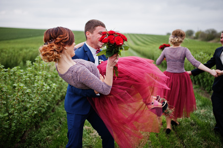 Handsome groomsmen holding bridesmaids and spinning them in blackcurrant field.の写真素材