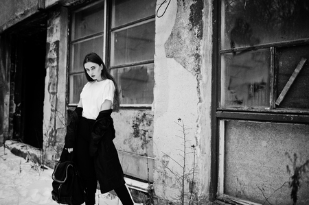 Fashionable long legs brunette model in long black cloak posed outdoor at winter day against old grunge wall with broken windows.の写真素材