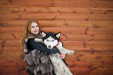 Red haired girl with husky dog against wooden wall.の写真素材