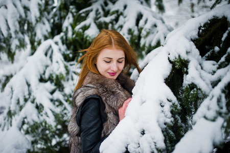 Red haired girl in fur coat walking at winter snowy park.