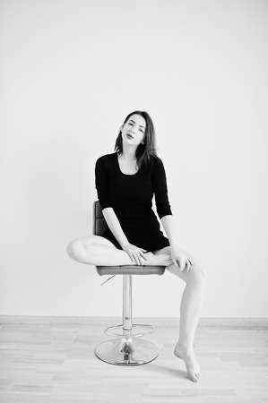 Red haired girl on black dress tunic sitting on red chair against white wall at empty room.の写真素材
