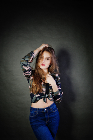 Handsome brunette girl wear military shirt and jeans, posing at studio against gray background. Studio model portrait.の写真素材