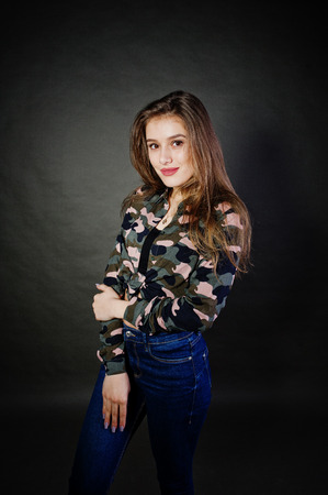 Handsome brunette girl wear military shirt and jeans, posing at studio against gray background. Studio model portrait.の写真素材