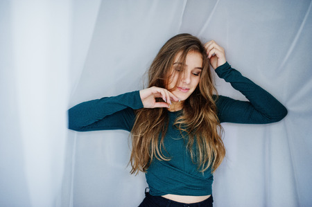 Handsome brunette girl wear on green, posing at curtains. Studio model portrait.