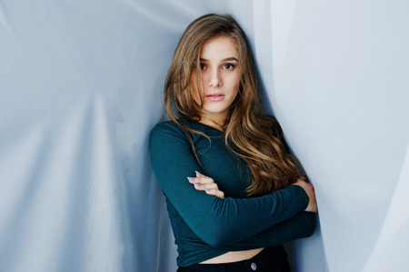 Handsome brunette girl wear on green, posing at curtains. Studio model portrait.