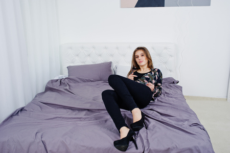 Handsome brunette girl wear military shirt, posing on bed at studio. Studio model portrait.の写真素材