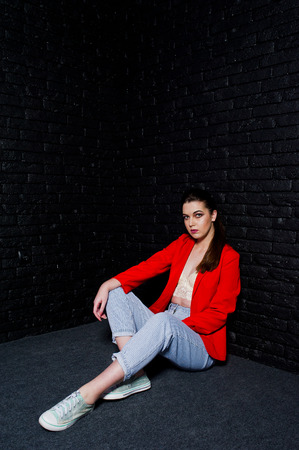 Stylish brunette girl on red jacket against studio black brick wall.の写真素材