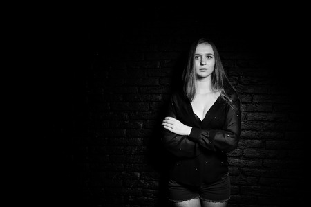 Studio shot of brunette girl in black blouse with bra and shorts against black brick wall.の写真素材
