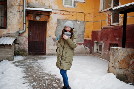 Portrait of brunette girl in gray scarf and hat, glasses at cold weather against orange wall of old house.の写真素材