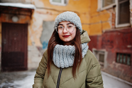 Portrait of brunette girl in gray scarf and hat, glasses at cold weather against orange wall of old house.の写真素材