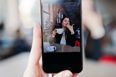Close up photo of screen mobile phones with brunette girl sitting on cafe with cup of cappuccino, listening music on headphones.の写真素材