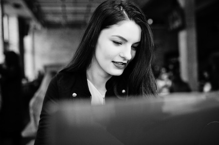 Brunette girl sitting on cafe and  working with red laptop.
