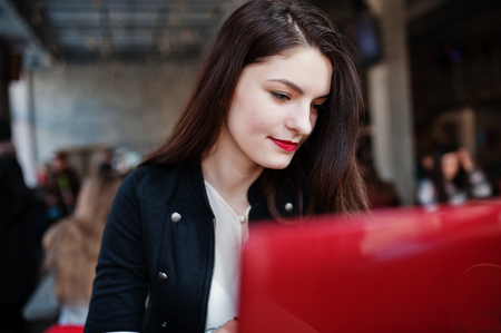 Brunette girl sitting on cafe and  working with red laptop.の写真素材