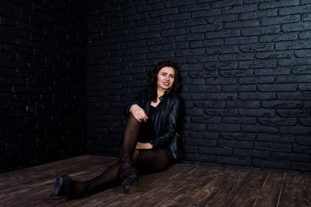 Studio portrait of sexy brunette girl in black leather jacket against brick wall.の写真素材