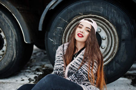 Brunette stylish casual girl in cap sitting against truck wheels.の写真素材