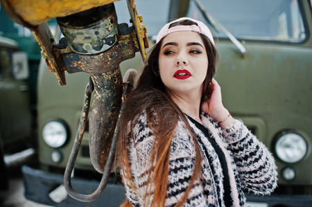 Brunette stylish casual girl in cap against old truck crane.の写真素材