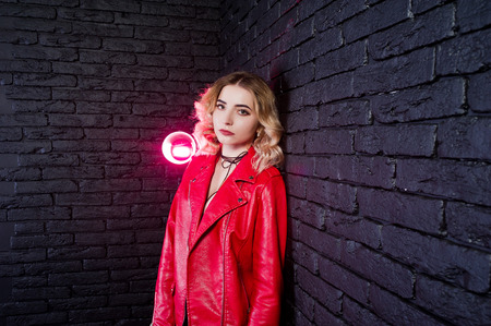 Studio portrait of blonde girl in red leather jacket against brick wall.の写真素材