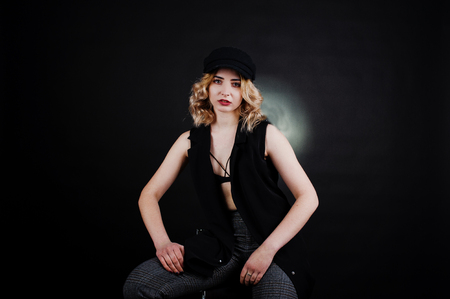 Studio portrait of blonde girl in black wear, bra and cap against dark background.の写真素材