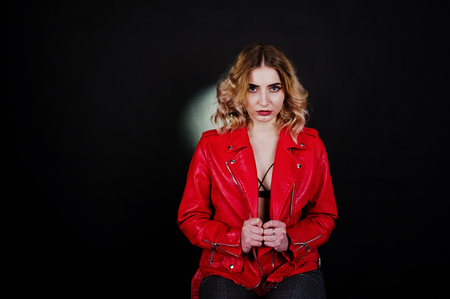 Studio portrait of blonde girl in red leather jacket against black background.の写真素材
