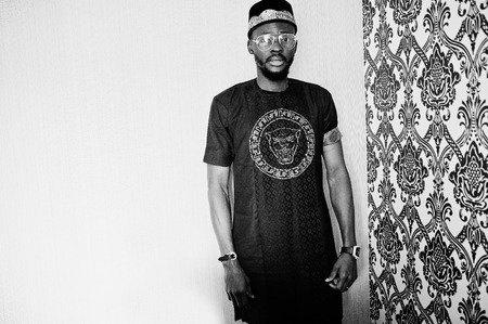 Rich african man in stylish traditional clothes and hat in glasses posed at studio against vintage...