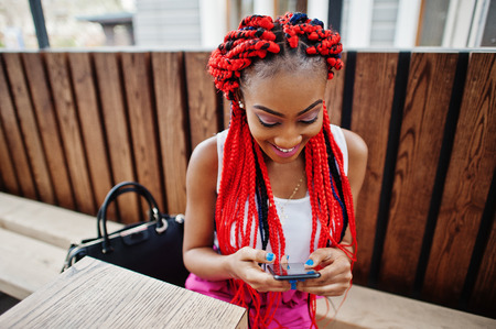 Fashionable african american girl at pink pants and red dreads posed outdoor with mobile phone.の写真素材
