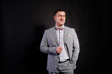 Studio portrait of man in gray suit and bow tie against black background.の写真素材