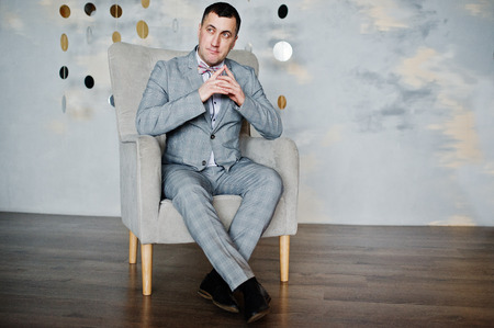 Studio portrait of man in suit near chair.の写真素材