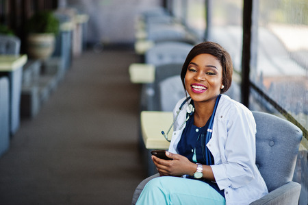 African american doctor female with stethoscope looked at phone and sitting on clinic.