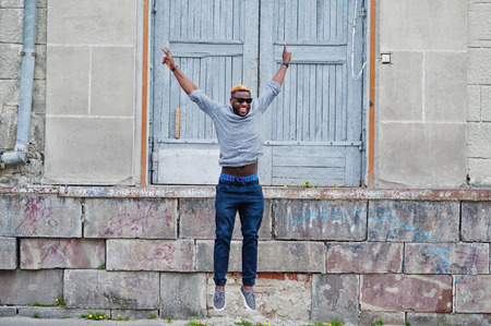 Stylish african american boy on gray sweater and black sunglasses posed on street. Fashionable black guy jump.の写真素材