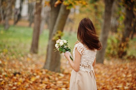 Amazingly girl bridesmaid in golden dress with bouquet at hands at autumn park.の写真素材