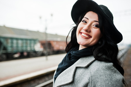 Brunette girl in gray coat with hat in railway station.