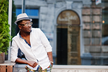 Stylish african american man in white shirt and colored pants with hat and glasses posed outdoor. Black fashionable model boy.の写真素材