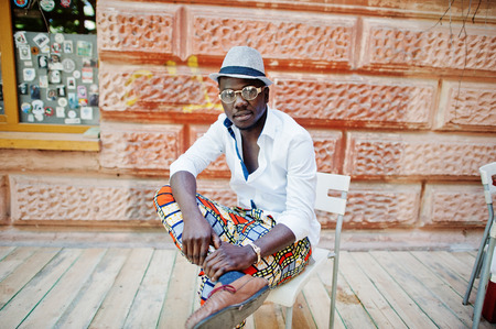 Stylish african american man in white shirt and colored pants with hat and glasses posed outdoor. Black fashionable model boy.の写真素材
