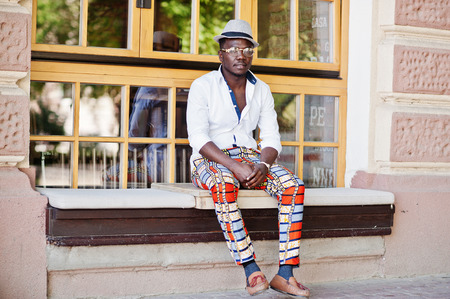 Stylish african american man in white shirt and colored pants with hat and glasses posed outdoor. Black fashionable model boy.の写真素材