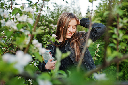 Young brunette girl at jeans against spring blossom tree with book.の写真素材