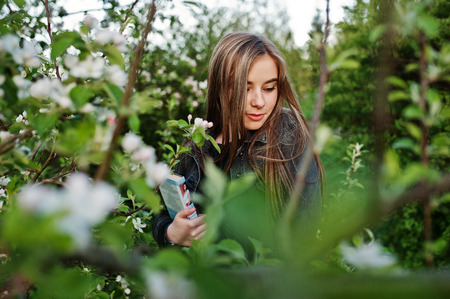 Young brunette girl at jeans against spring blossom tree with book.