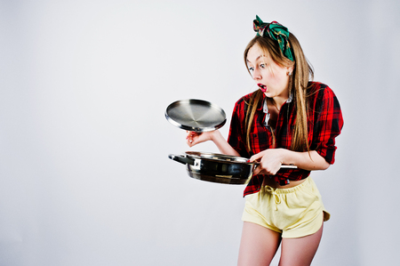 Young funny housewife in checkered shirt and yellow shorts pin up style with frying pan isolated on white background.の写真素材
