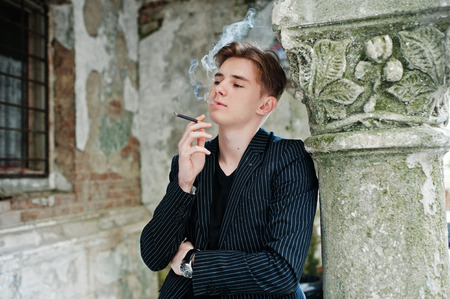 Young macho boy wear on blac stylish jacket smoking cigarette on streets.の写真素材