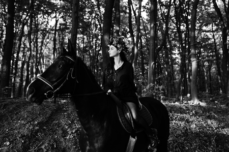 Mystical girl in wreath wear in black at horse in wood.の写真素材