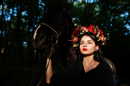 Mystical girl in wreath wear in black with horse in wood.の写真素材