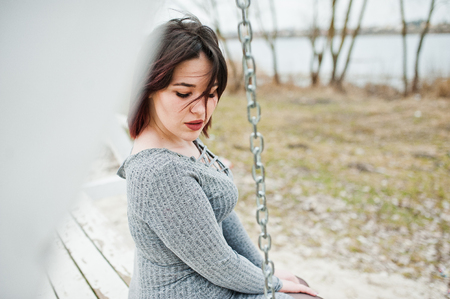Portrait of brunette girl in gray dress sitting at white wooden construction.の写真素材