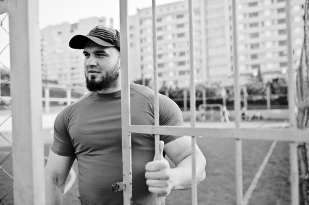 Young brutal bearded muscular man wear on red shirt, shorts and cap at stadium.の写真素材