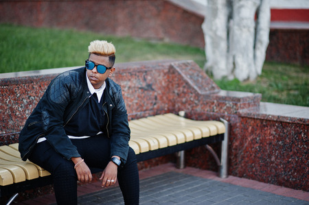 Stylish arabian muslim boy with originally hair and sunglasses posed on streets, sitting on bench.の写真素材