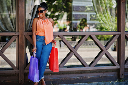 Casual african american girl with colored shopping bags walking outdoor. Stylish black woman shopping.の写真素材