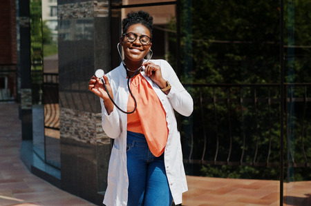 African american doctor female at lab coat, glasses with stethoscope posed outdoor against clinic.の写真素材