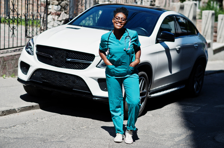 African american doctor female at lab coat with stethoscope posed outdoor against white suv car.の写真素材
