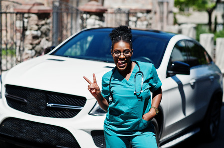 African american doctor female at lab coat with stethoscope posed outdoor against white suv car.の写真素材