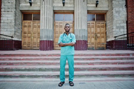African american doctor male at lab coat with stethoscope outdoor against clinic door.の写真素材