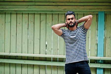 Handsome tall arabian beard man model at stripped shirt posed outdoor against wooden background....