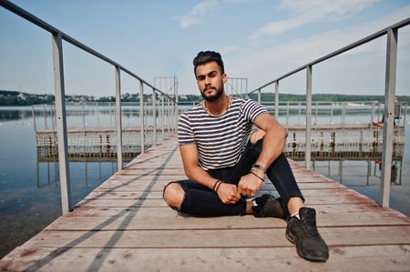 Handsome tall arabian beard man model at stripped shirt posed outdoor on pier of lake. Fashionable arab guy.の写真素材